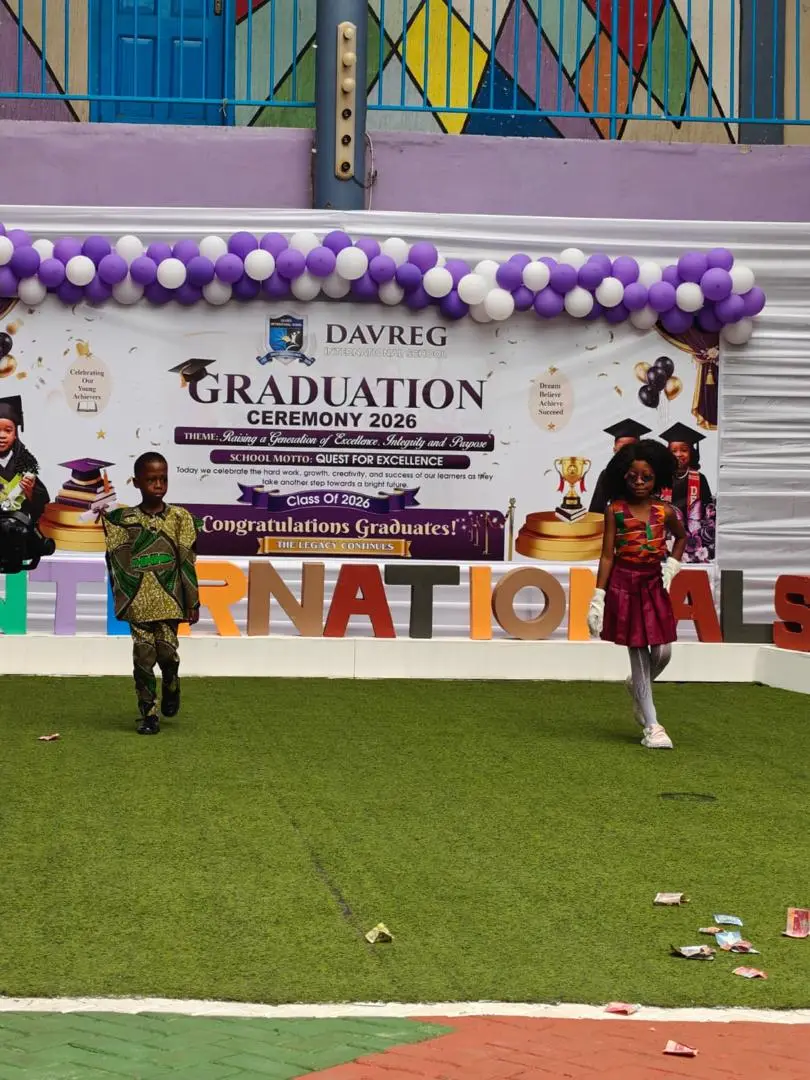 Two pupils walking the runway in traditional outfits in front of the Graduation Ceremony 2026 banner