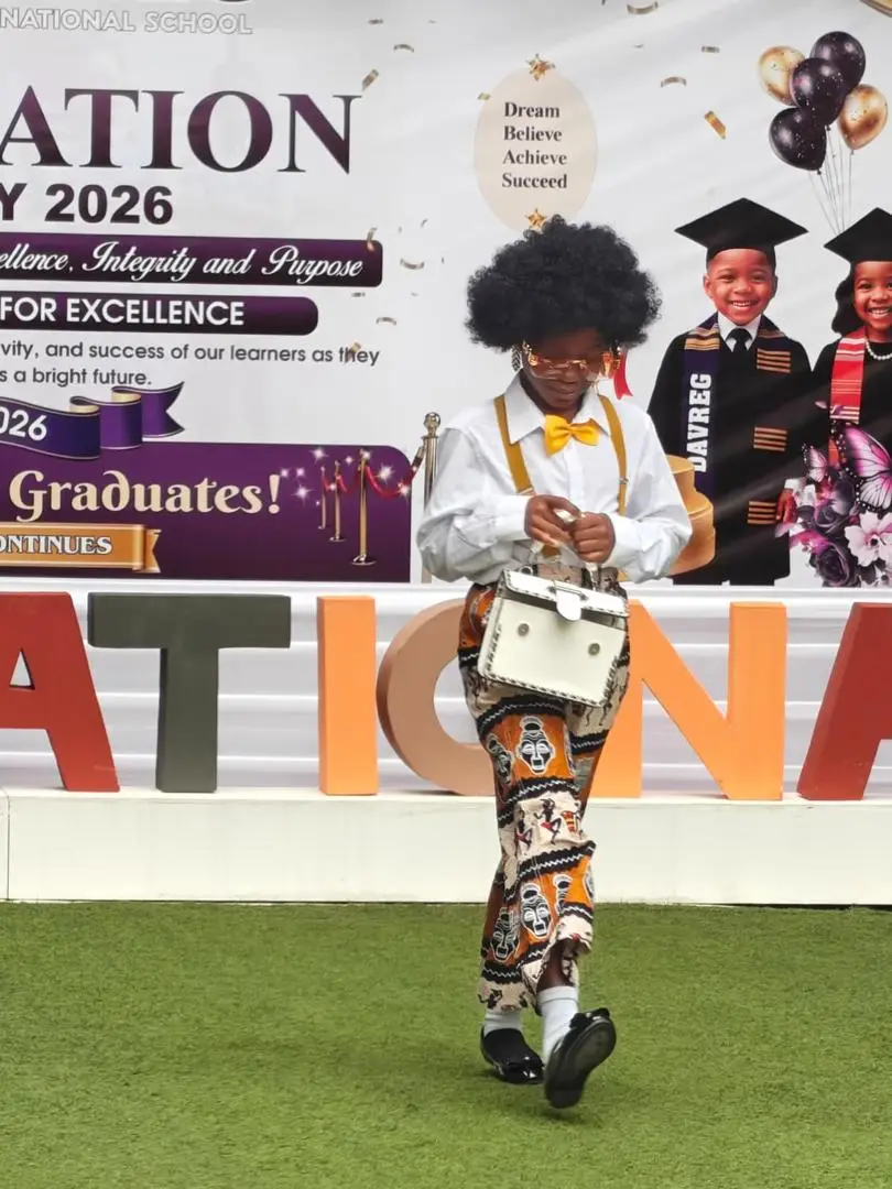 A pupil in a yellow bow tie and braces carrying a vintage handbag on the runway