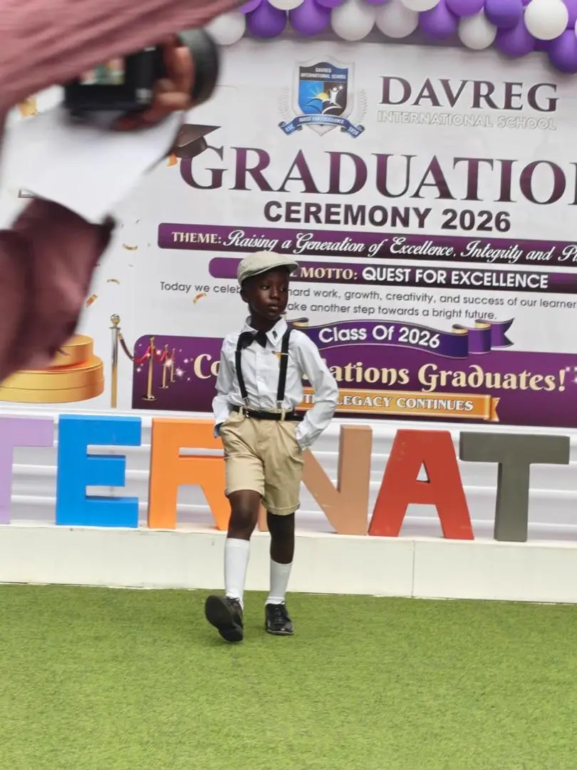 A pupil in a flat cap, bow tie and braces walking the runway