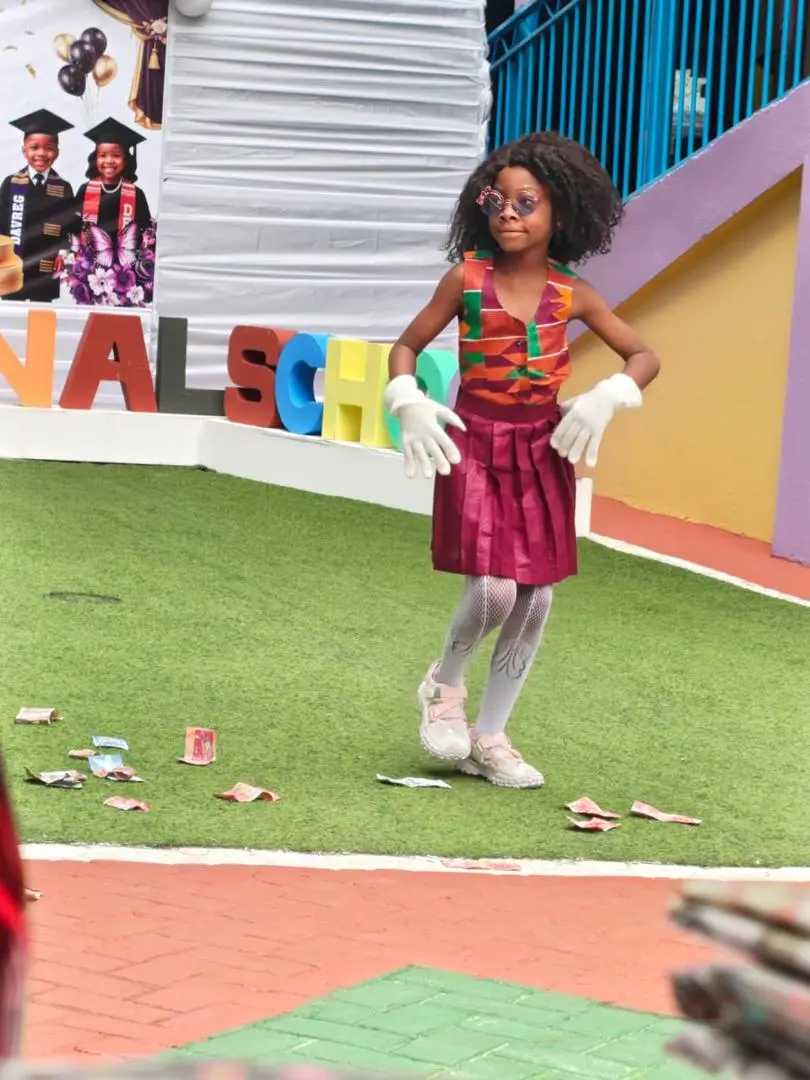 A pupil in a kente top and white gloves dancing on the runway