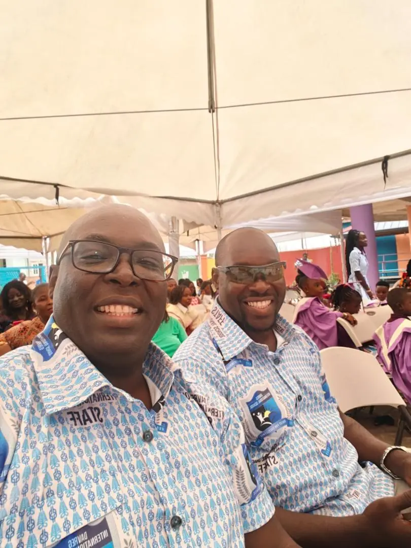Two DavReg staff members in school staff shirts at the ceremony, with graduates seated behind them